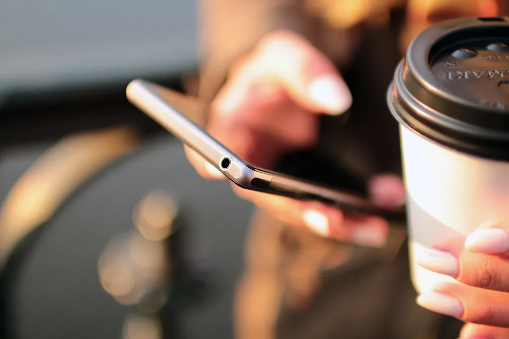 Mãos segurando um celular, com um copo de café ao lado