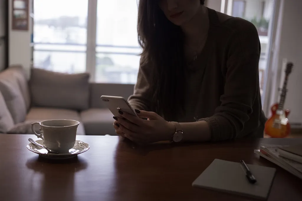 Pessoa lendo uma mensagem no celular, sentada à mesa